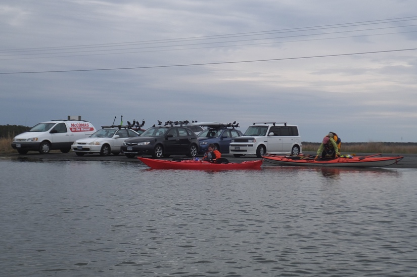 Vehicles staged in lot with kayakers preparing to launch