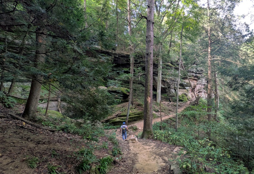 Daphne and I walking on a dirt trail lined by trees, low vegetation, and rock formations