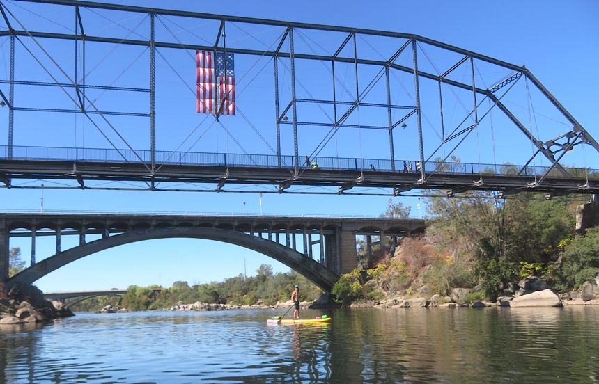Me on SUP with two bridges behind; the one in the front has a big American flag hanging from it