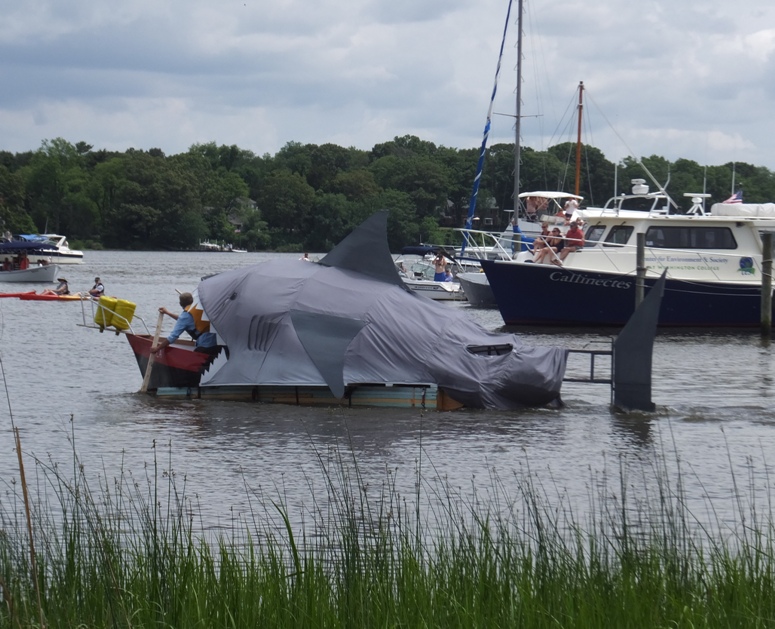Raft resembling a large shark chasing a small boat
