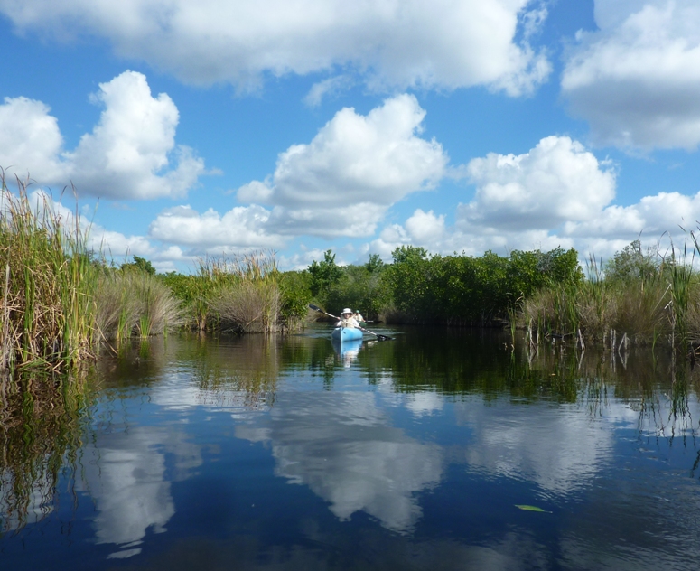 Norma kayaking with Carmen behind; waterway lined by grasses