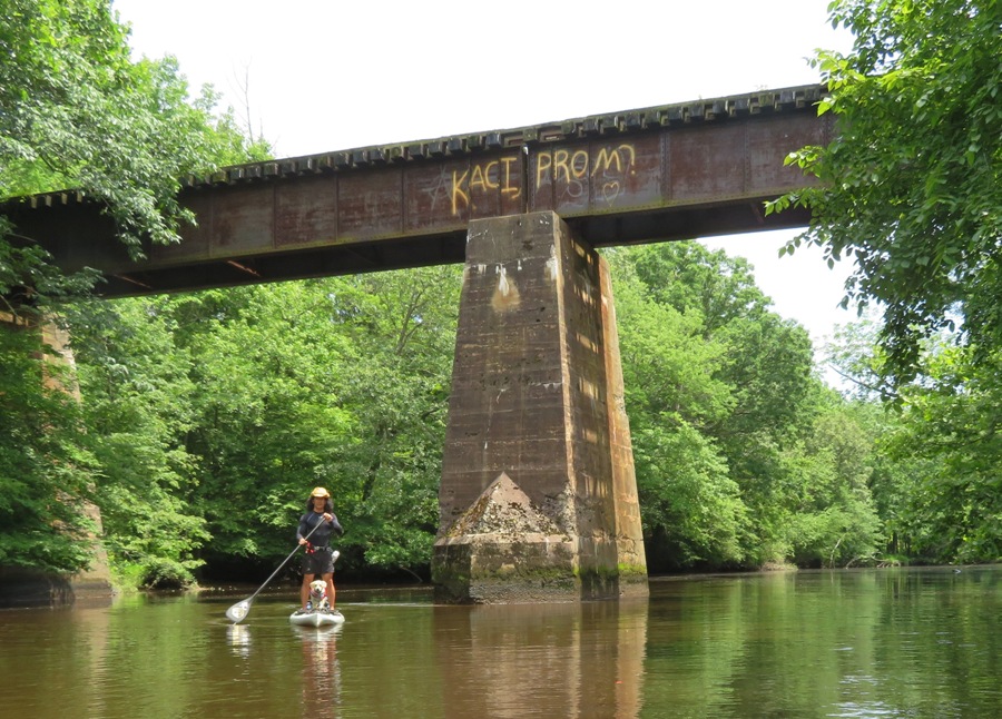 Daphne and me on SUP under bridge that reads 'Kaci Prom?'