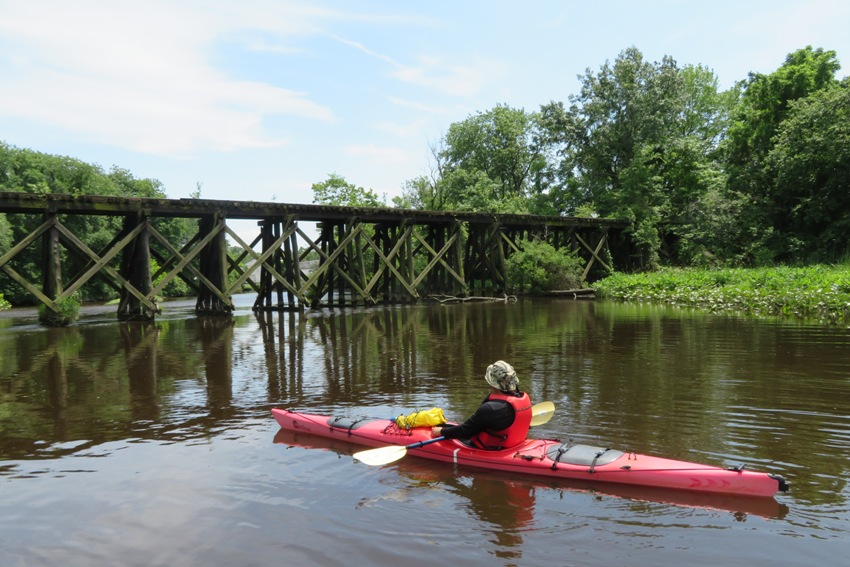 Steve in kayak in front of old, wooden train bridge