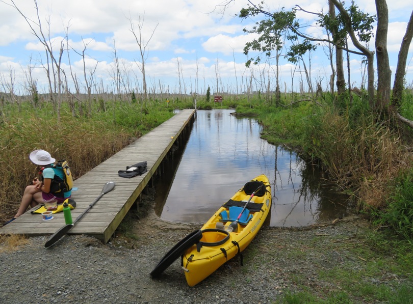Norma sitting on the pier eating with the kayak on the shore