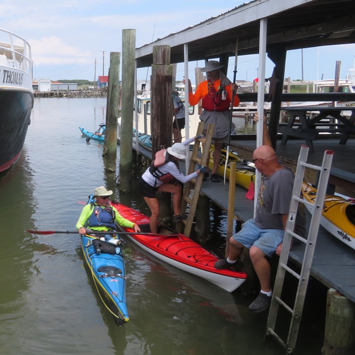 Anisa climbing down ladder to get into her boat with Dr. Greg in his kayak