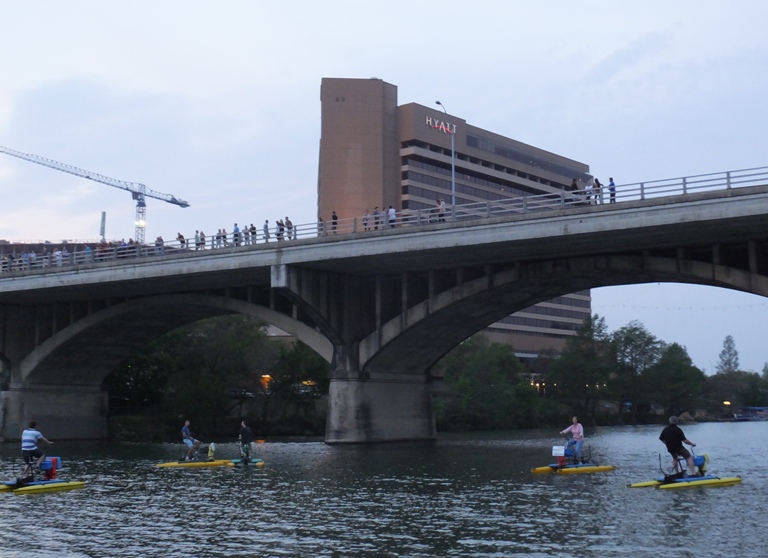 People on bicycle boats by bridge