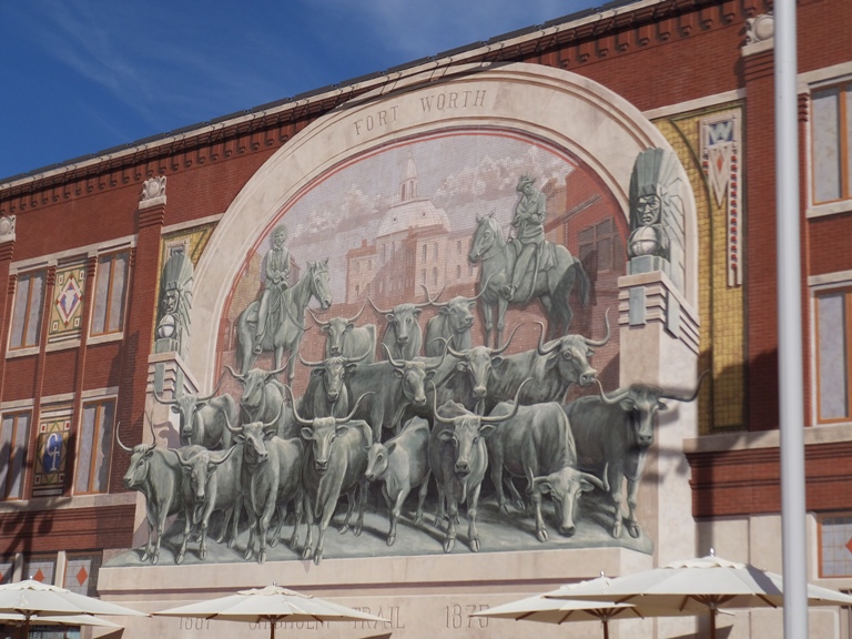 A mural o the side of a building showing lots of longhorn cattle