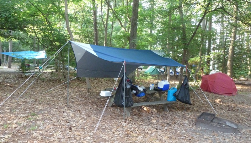 Red tent and dark gray-green sun shade over picnic table with trash bags