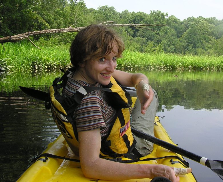 Norma on kayak with fuzzy caterpillar on her wrist and thumbs wrapped in tape