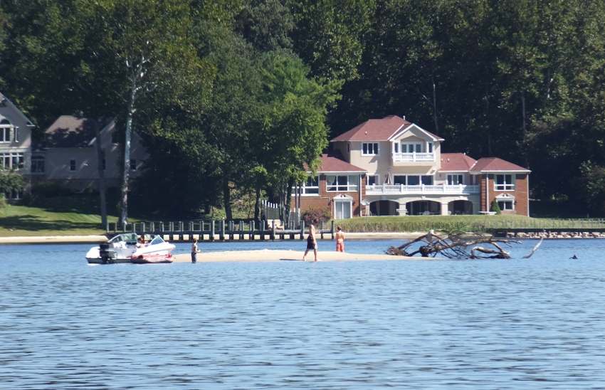 Three people on tiny sandy island with fallen tree and power boat