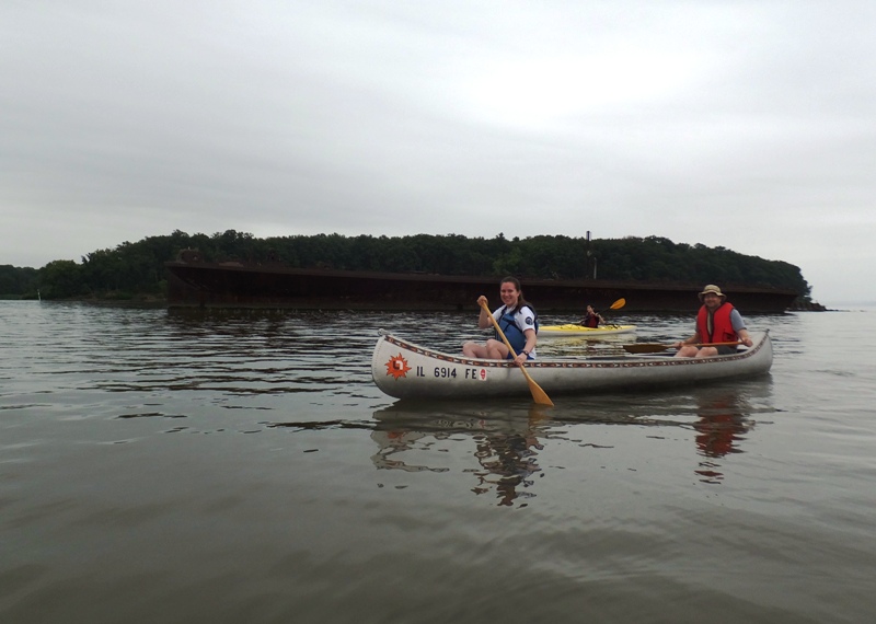 Sam and Don in a canoe with Chandler and wreck behind