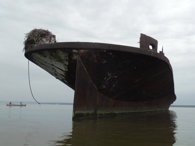 Metal ship with osprey nest on top and canoe in the background
