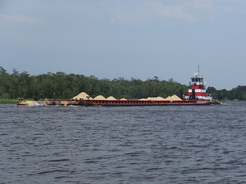 Tug boat pushing platform full of what looks like sand