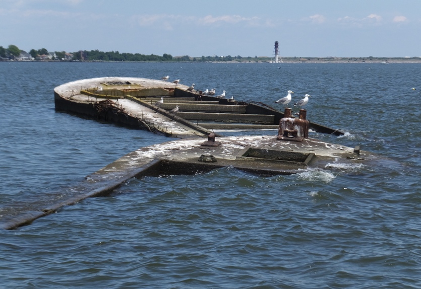 Two concrete barges with seagulls perches and the Craighill Channel Lower (Range) Rear Lighthouse in the distance