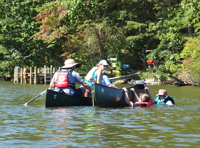 Boys in water hanging onto side of canoe with educators in canoe next to them