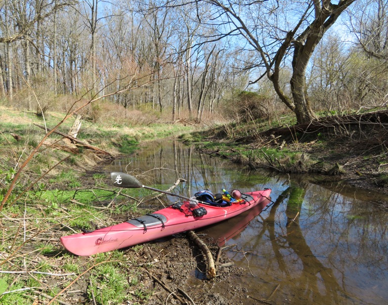 My red kayak on shore of narrow creek with paddle on top