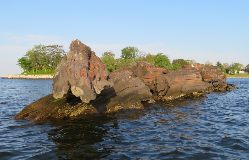 Several large rocks sticking out of the water with the leftmost appearing to be balanced on another rock