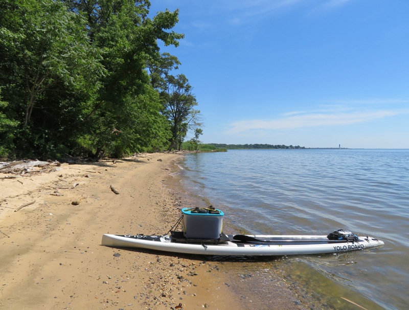 My SUP on shore with box containing my drone and lighthouse in the distance