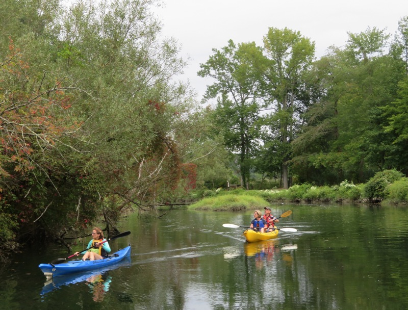 Norma, Beate, and Gerhard kayaking with a walking trail in the background