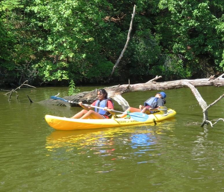 Two of Malar's daughters kayaking with one ducking under log