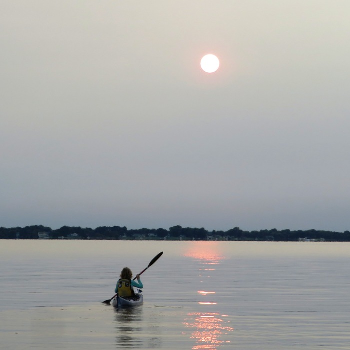 Norma kayaking on smooth water with sun in sky