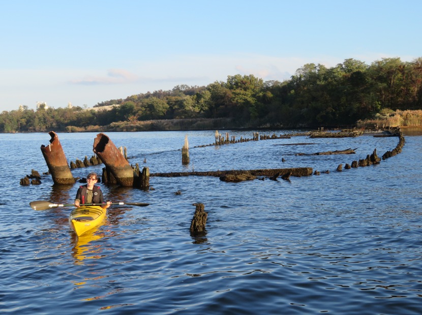 Sara in kayak with wreck behind