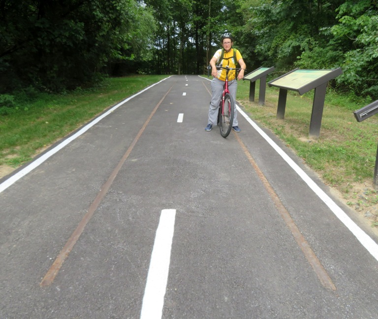 Norma on bicycle on section of trail showing railroad tracks through the pavement
