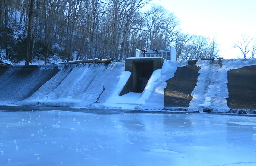 Water running over the concrete mill dam with ice